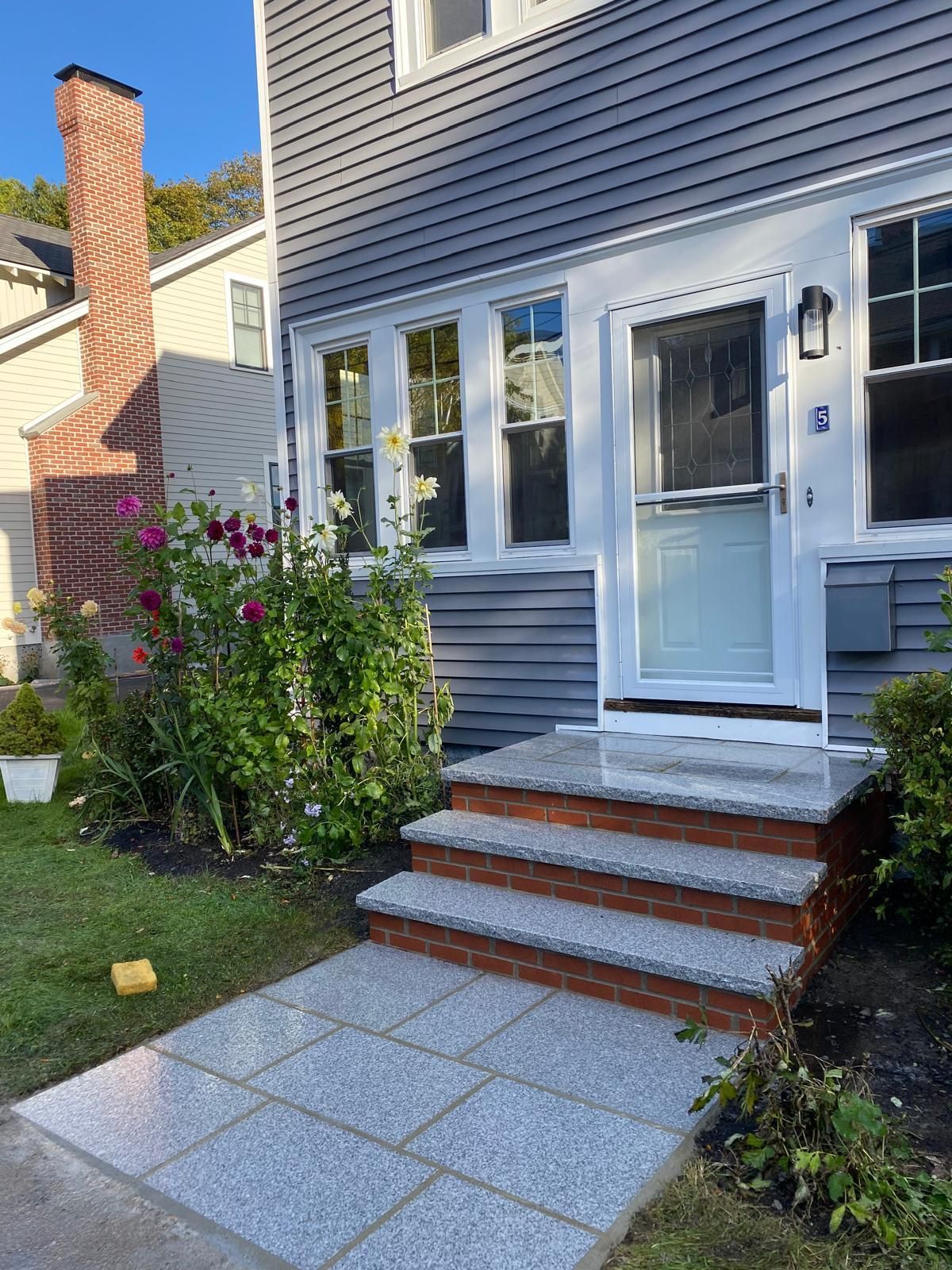 Exterior view of a house with a gray facade, brick steps, and a paved walkway leading to the front door.