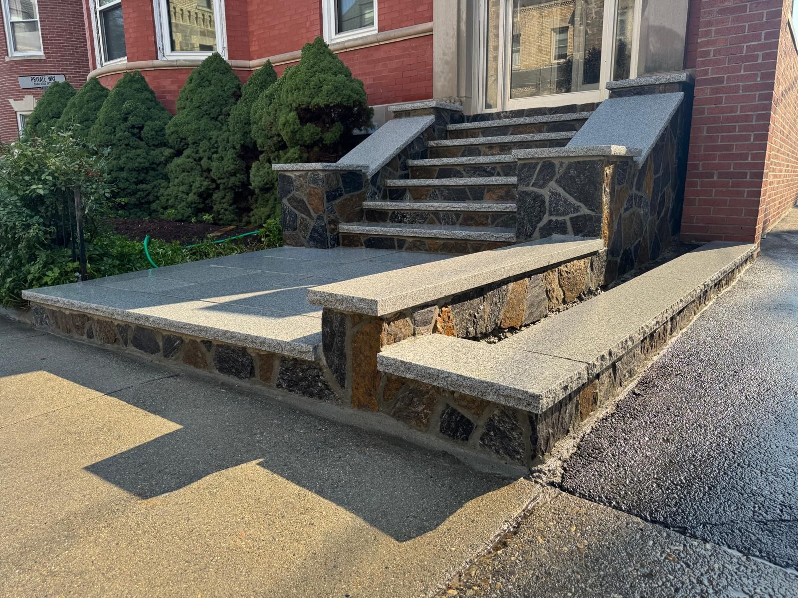 Stone steps and landing leading to a building's entrance. Black stone accents the concrete.