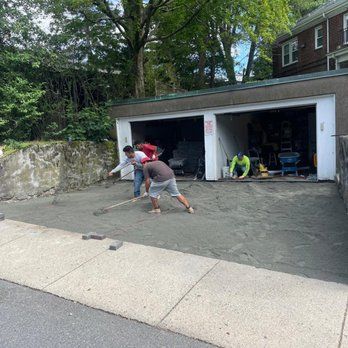 Workers leveling gravel in front of a two-car garage. They use rakes.