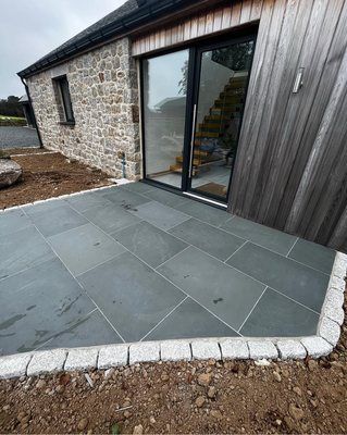 Stone patio with gray flagstones and granite border next to a building with glass doors.
