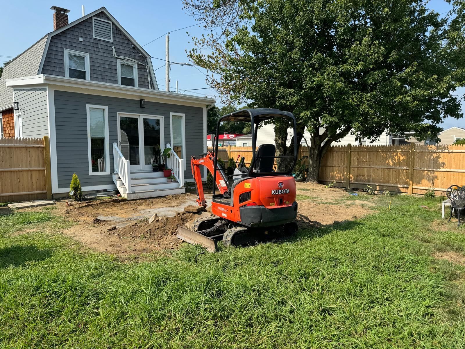 Small orange excavator in a backyard near a house with gray siding.