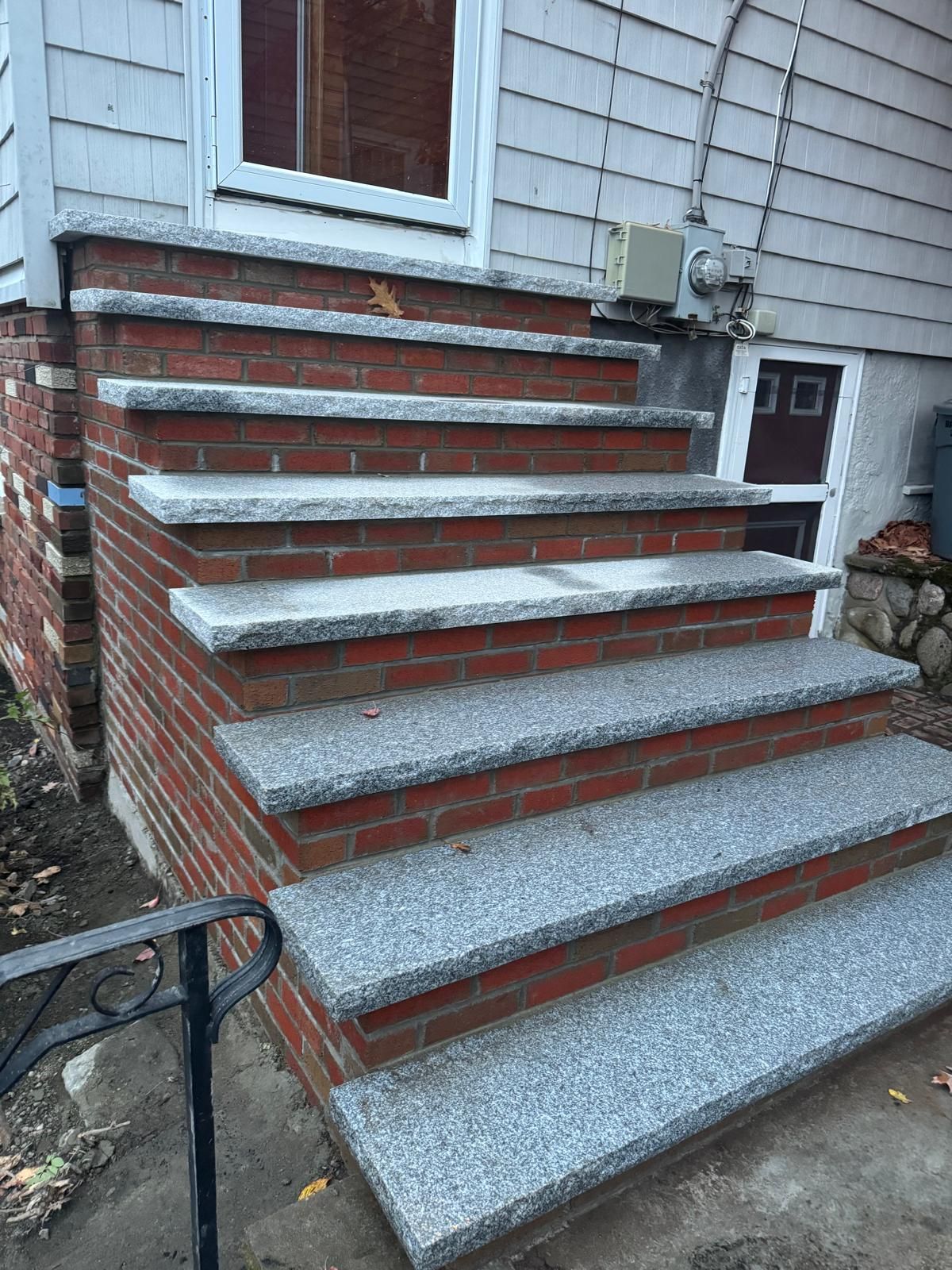 Brick steps with gray granite treads leading to a white door. Exterior of a house.