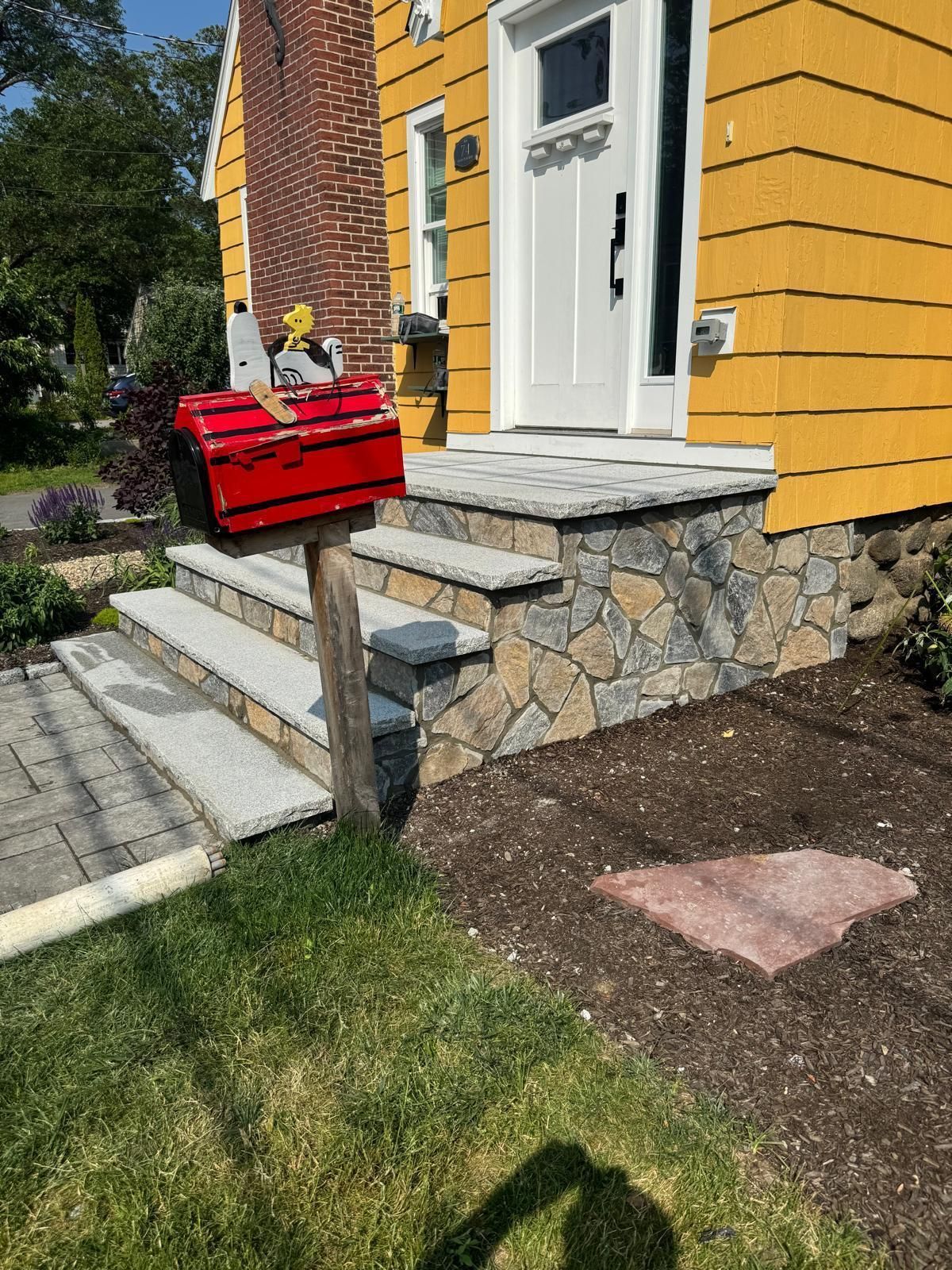 Red mailbox on wooden post next to steps leading to yellow house entrance.
