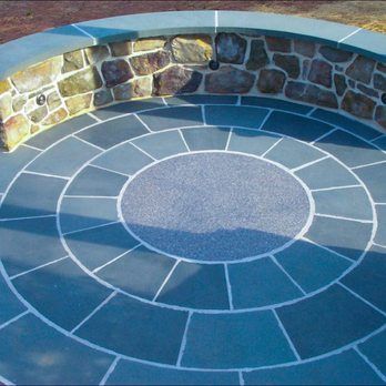 Circular stone patio with a stone wall backdrop and gray stone and grout design.