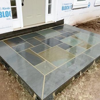 Stone front porch with dark blue-gray tiles in a geometric pattern, beside a white door.