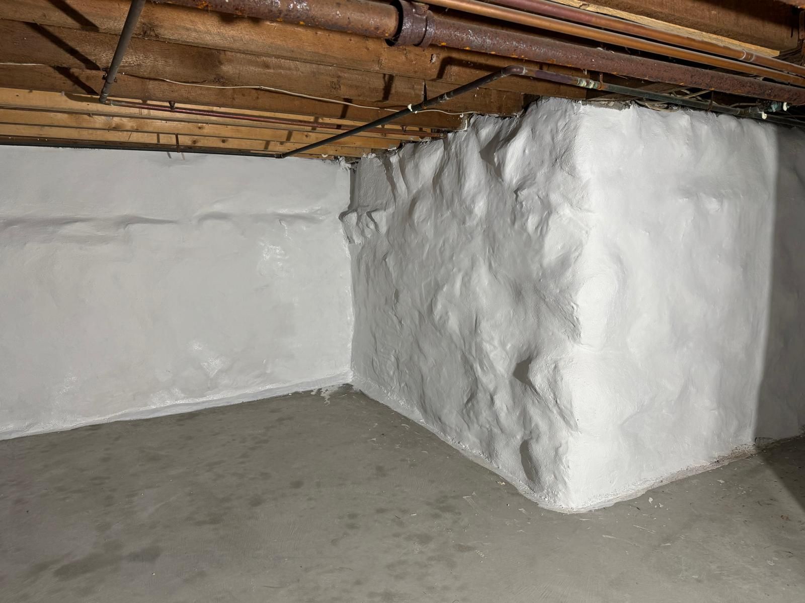 White-painted stone and concrete basement walls with exposed pipes and joists overhead.