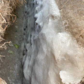 Foamy, grey substance filling a narrow trench between dirt and rock.