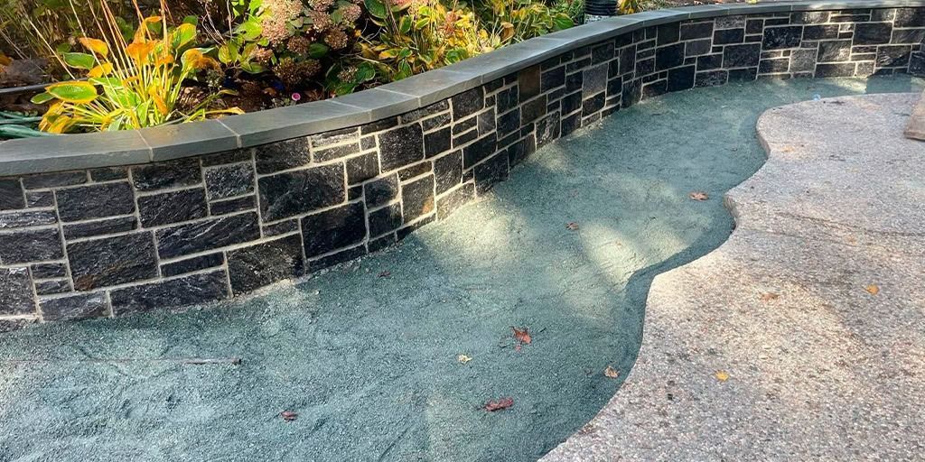 Curved stone wall with a pathway of blue-green gravel.