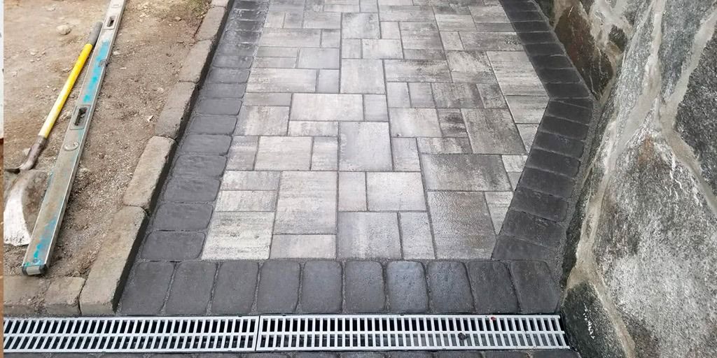 Pathway with paving stones, border, and a drain against a stone wall.