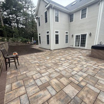 Backyard patio with patterned pavers, a house, and a hot tub.