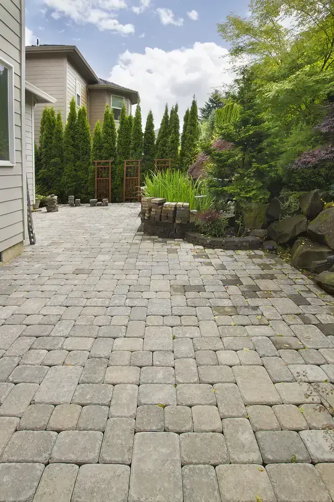 Brick patio with a house, tall trees, and garden.