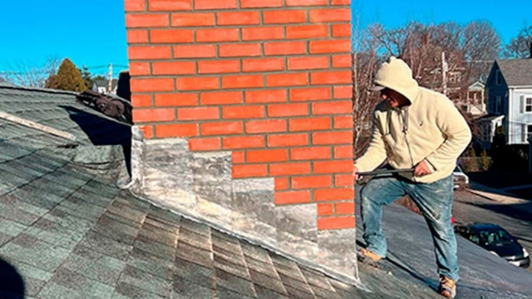 Person on a roof near a brick chimney repairing flashing. Sunny day, urban setting.