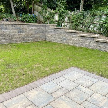 Stone patio in front of a yard with grass and retaining walls, and steps leading up.