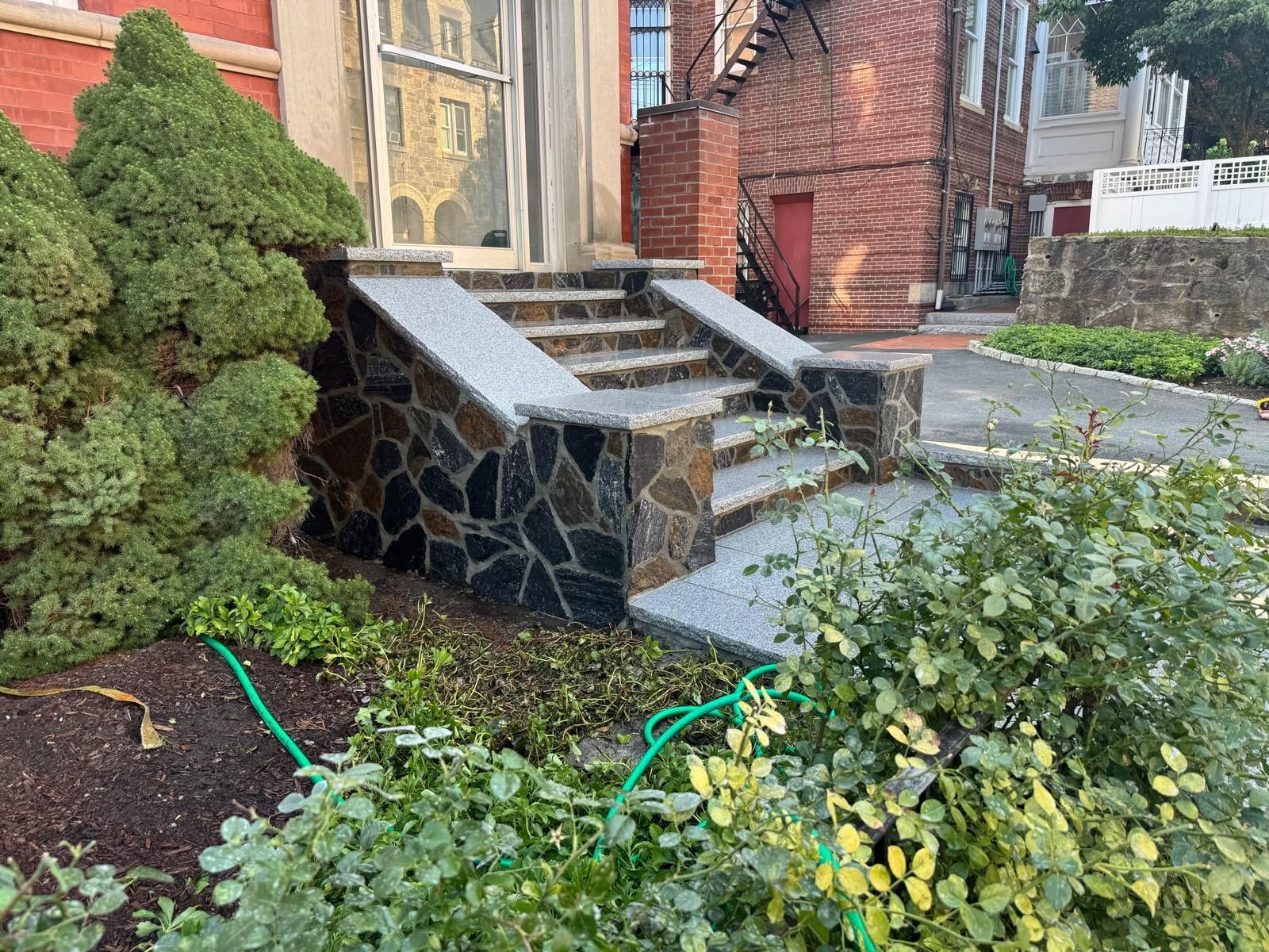 Stone steps leading up to a building entrance, bordered by a dark stone wall and landscaping.