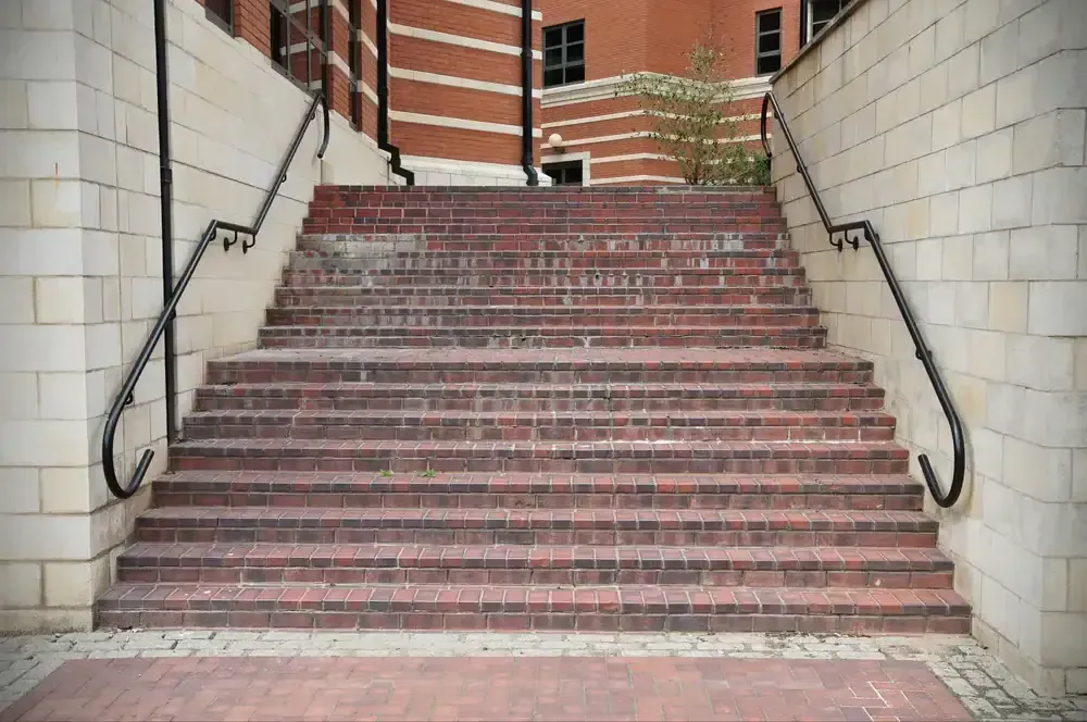 Brick staircase with black handrails ascending towards a building with windows, set between white brick walls.