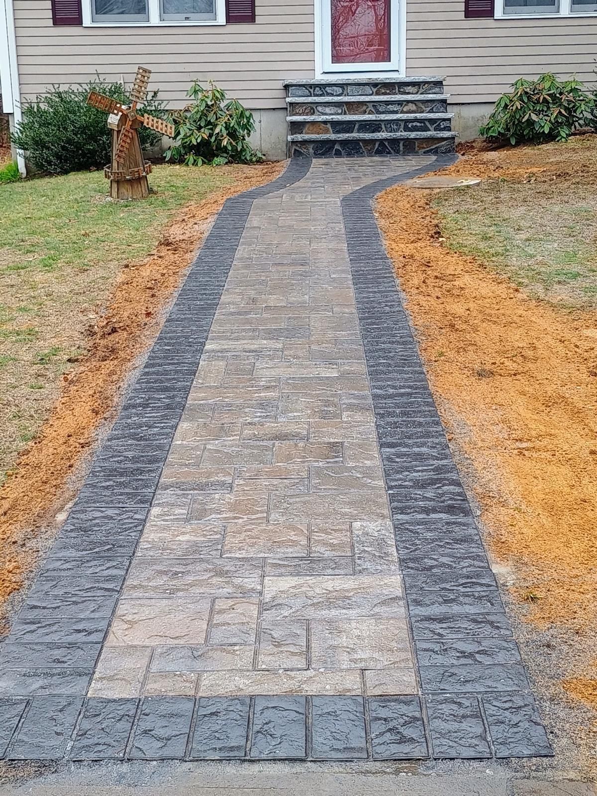 Paver pathway leading to a house entrance with stone steps. Pathway has dark borders and light center.