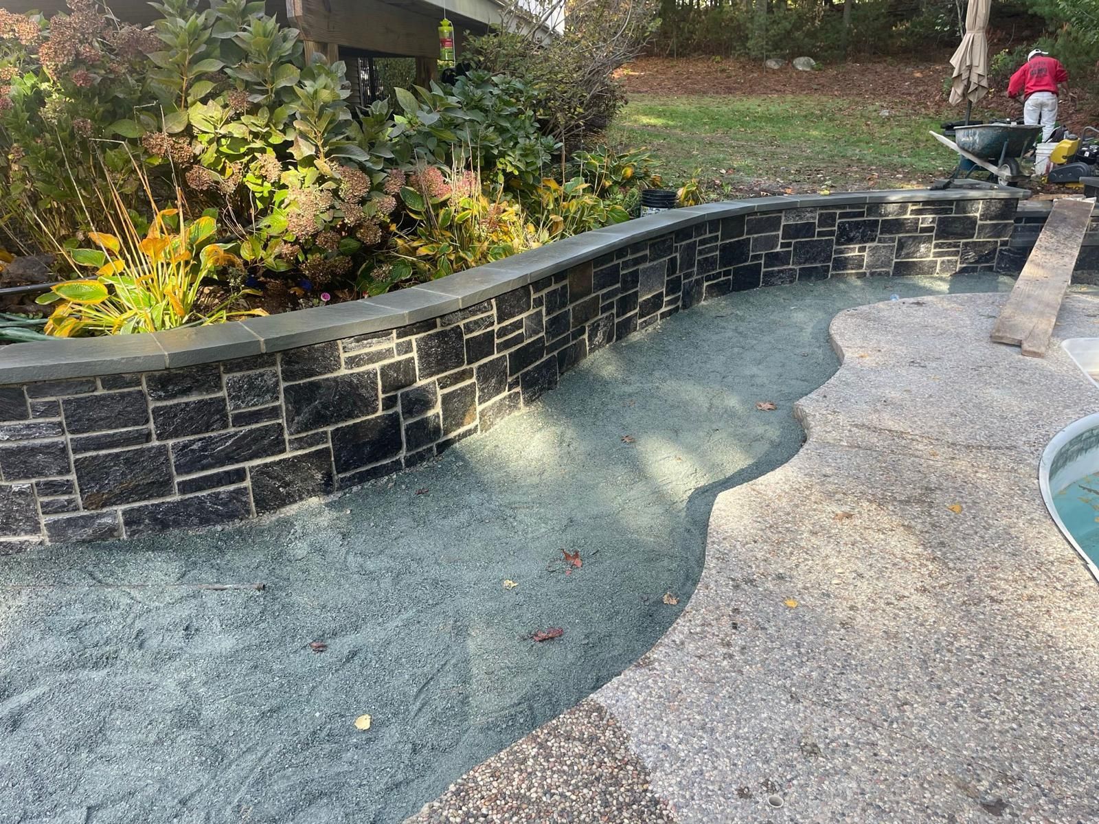 Black stone retaining wall bordering gravel and a pool deck.