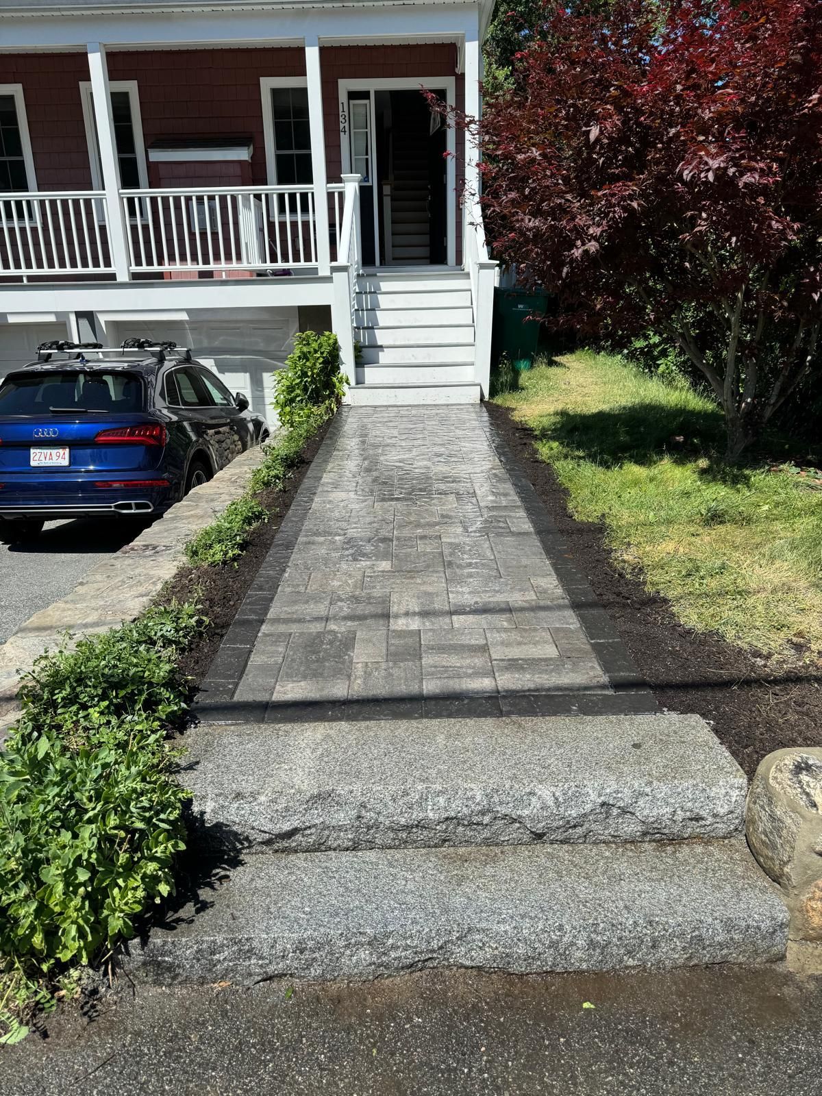 Stone path and steps leading to a house entrance. Includes driveway, bushes, and a car.