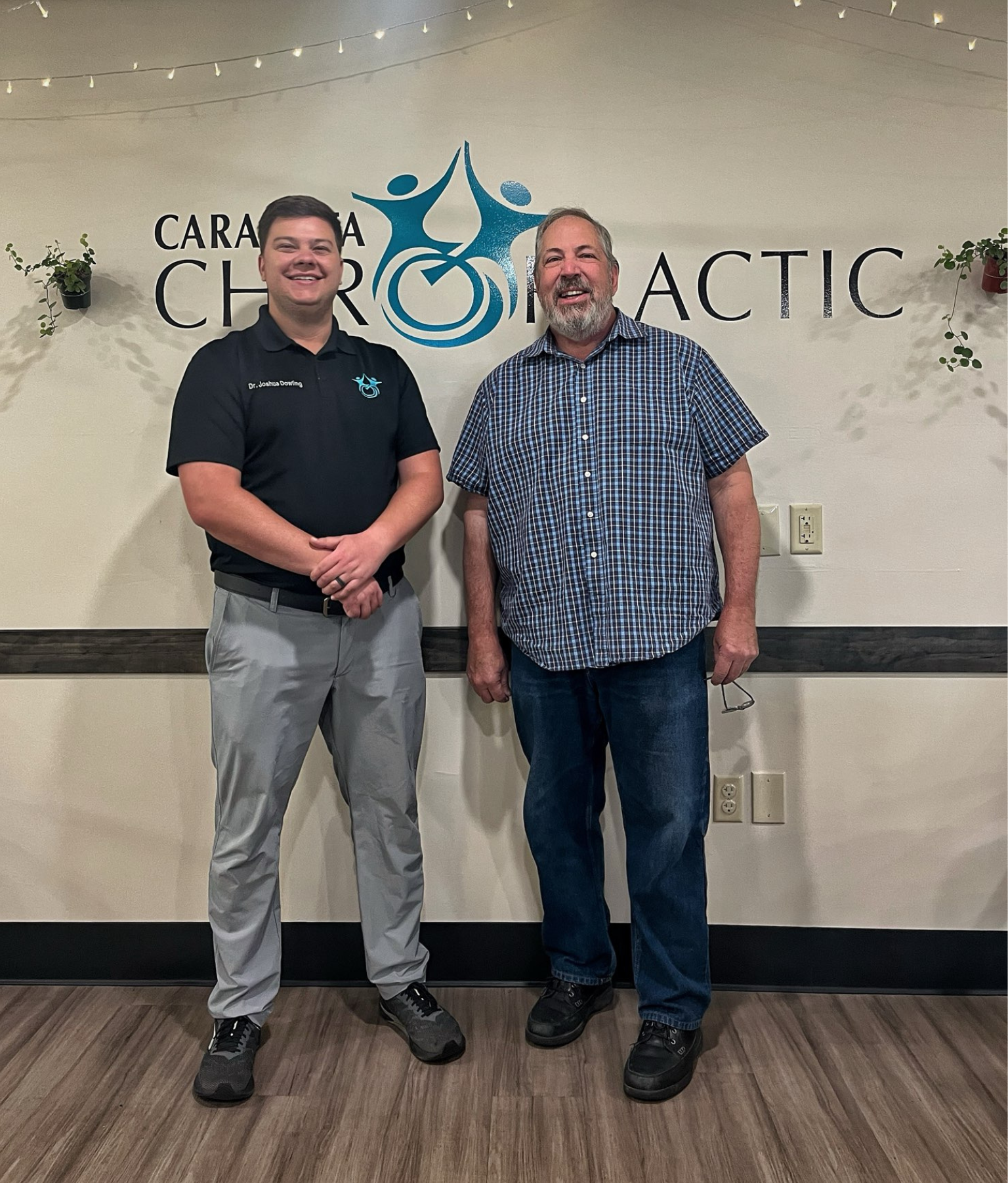 Two men standing and smiling in front of a Carolina Charter Academy sign.
