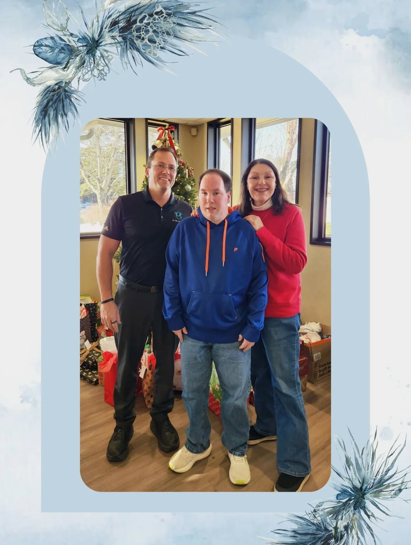 Three people standing together indoors, smiling, with a window and holiday decorations behind them