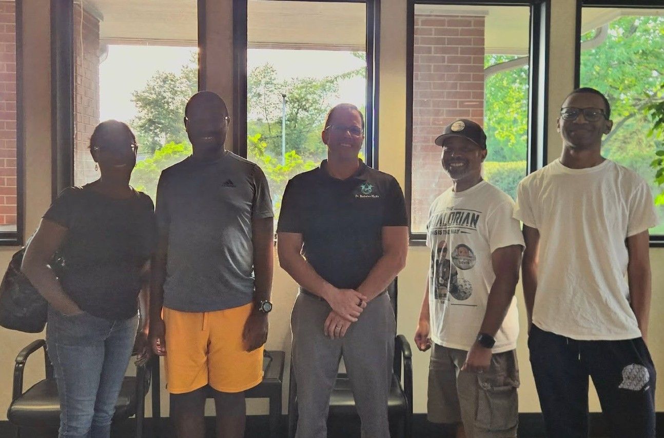 Five people standing indoors in front of large windows, posing for a group photo.
