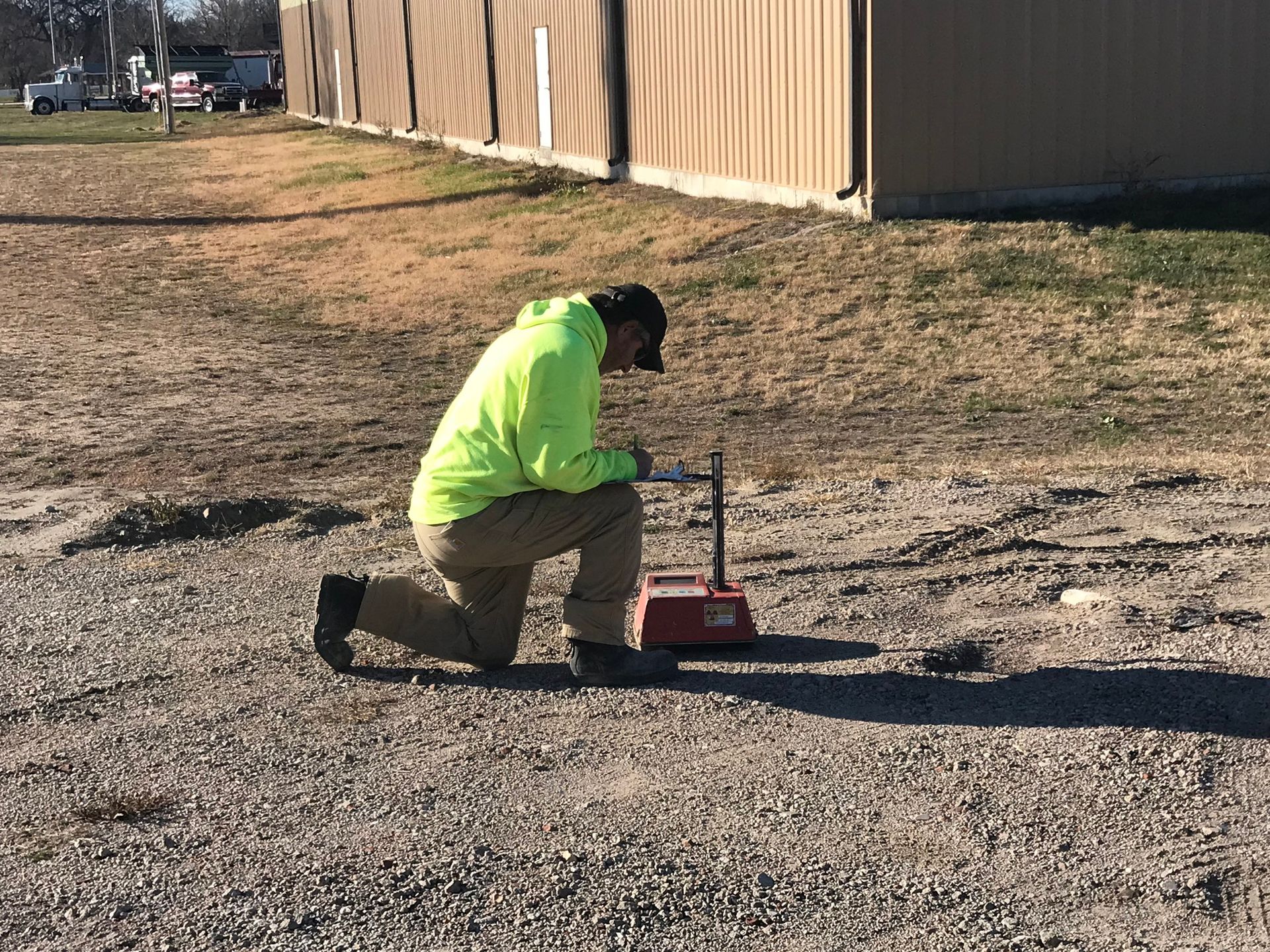 A man in a neon green jacket is kneeling down in the dirt.