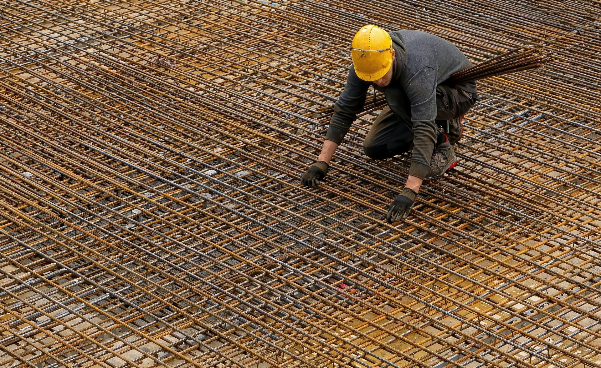A construction worker wearing a hard hat is working on a metal mesh.