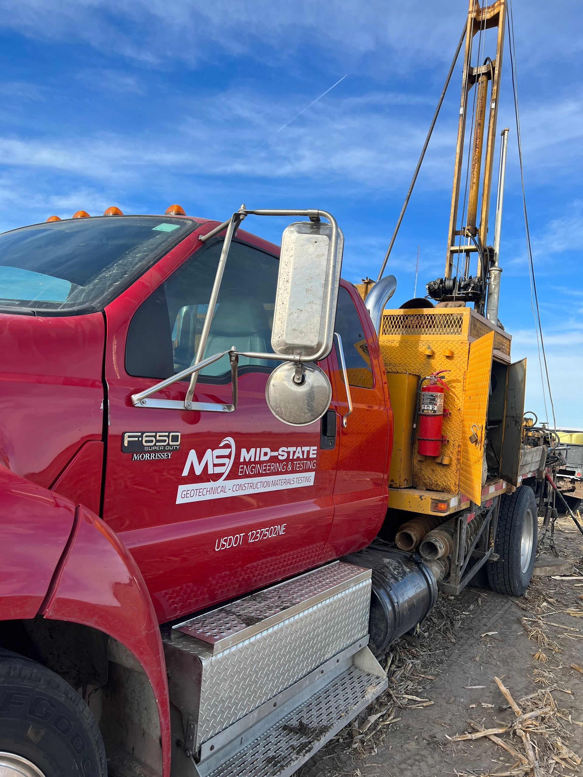 A red truck with a yellow crane attached to it is parked in a field.