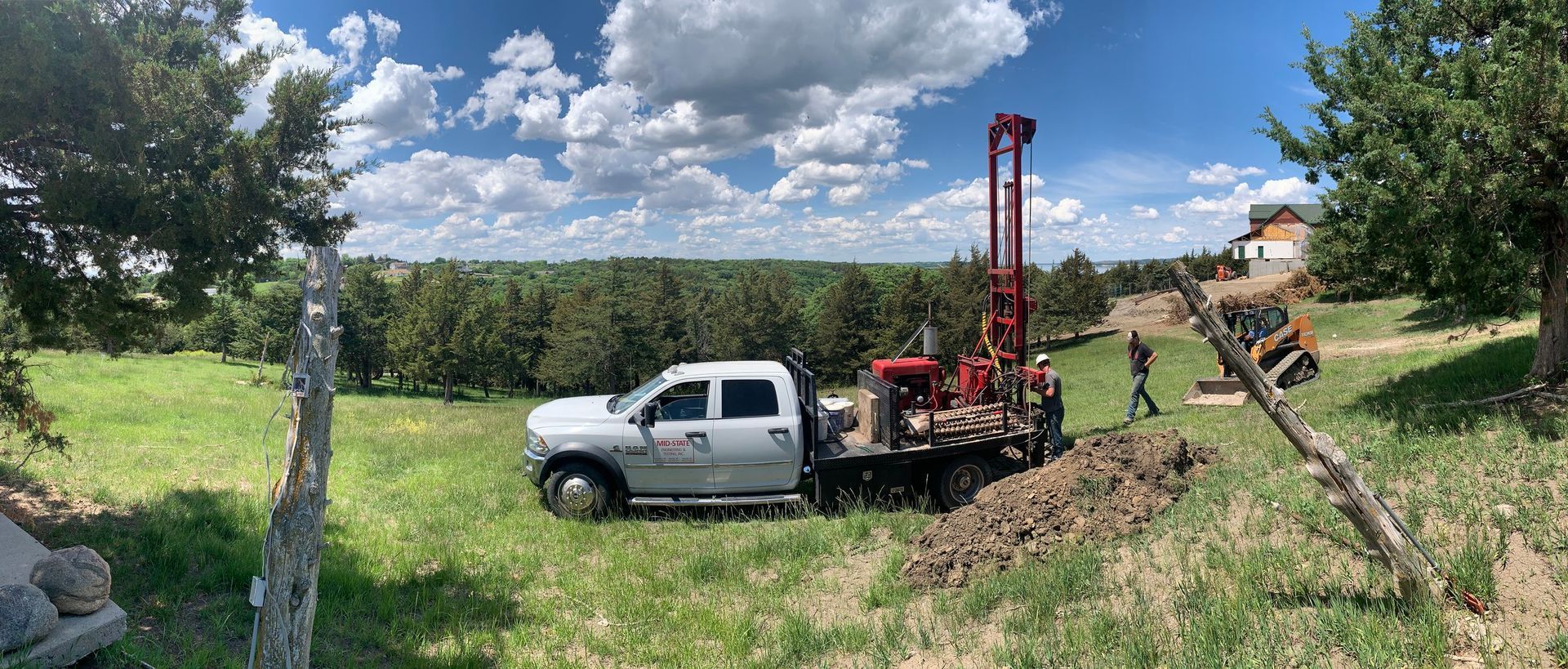 A white truck is parked in a grassy field next to a drilling rig.