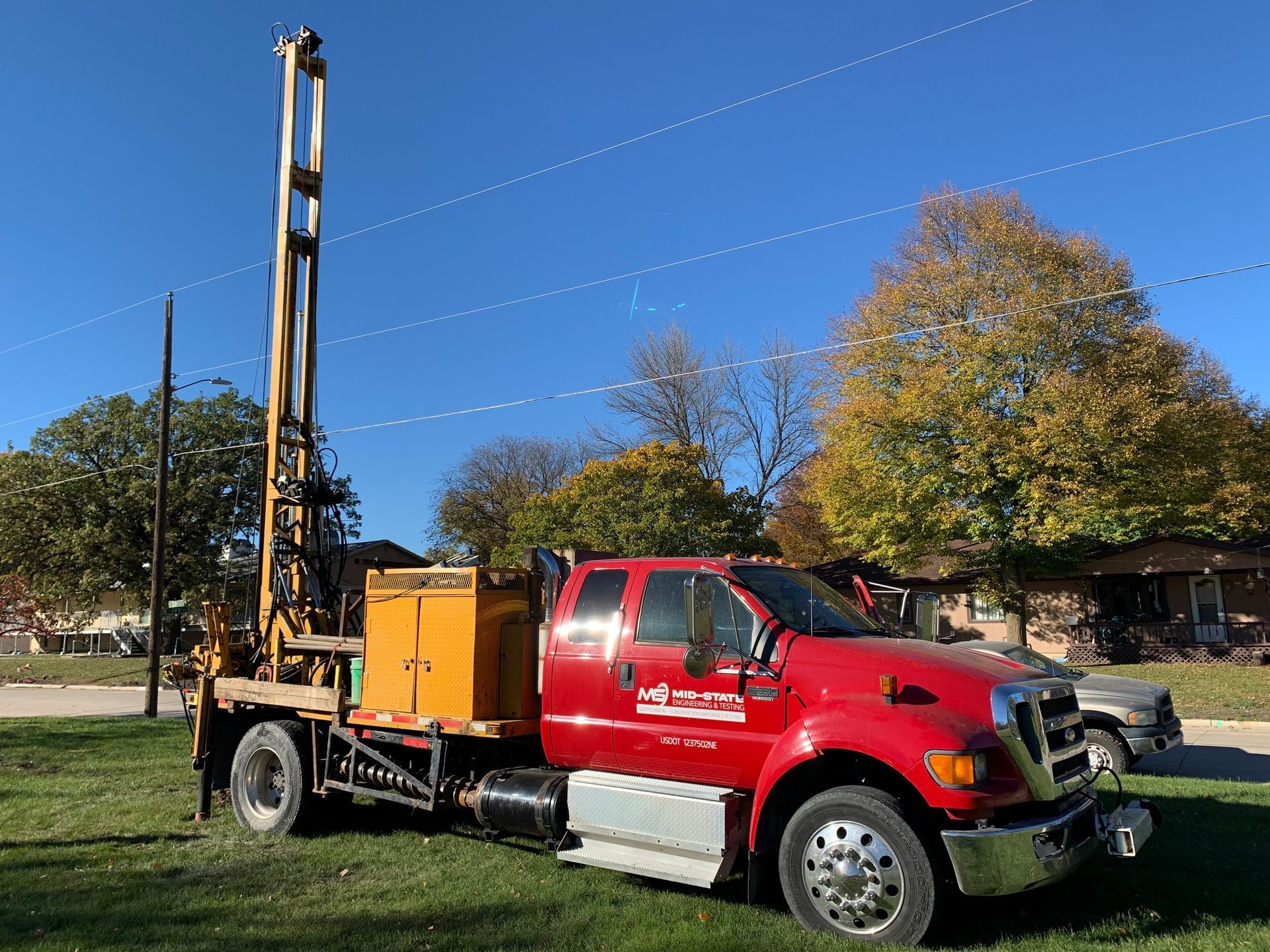 A red truck with a drilling rig on the back is parked in a grassy field.