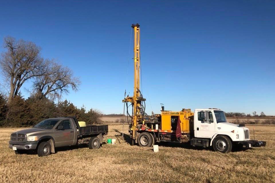 A truck is parked next to a drilling rig in a field.
