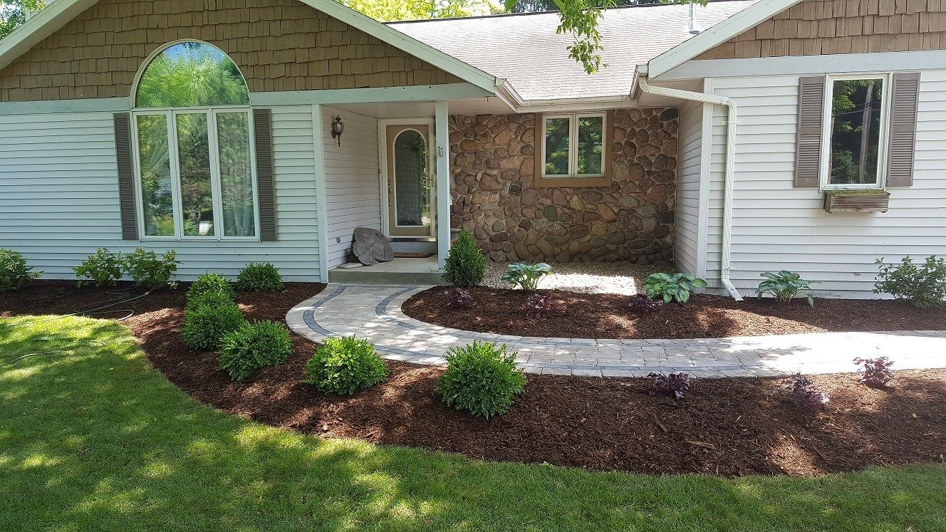 A ranch-style house with white siding, brown shingles, and stone accents, featuring a curved stone path and fresh mulch.