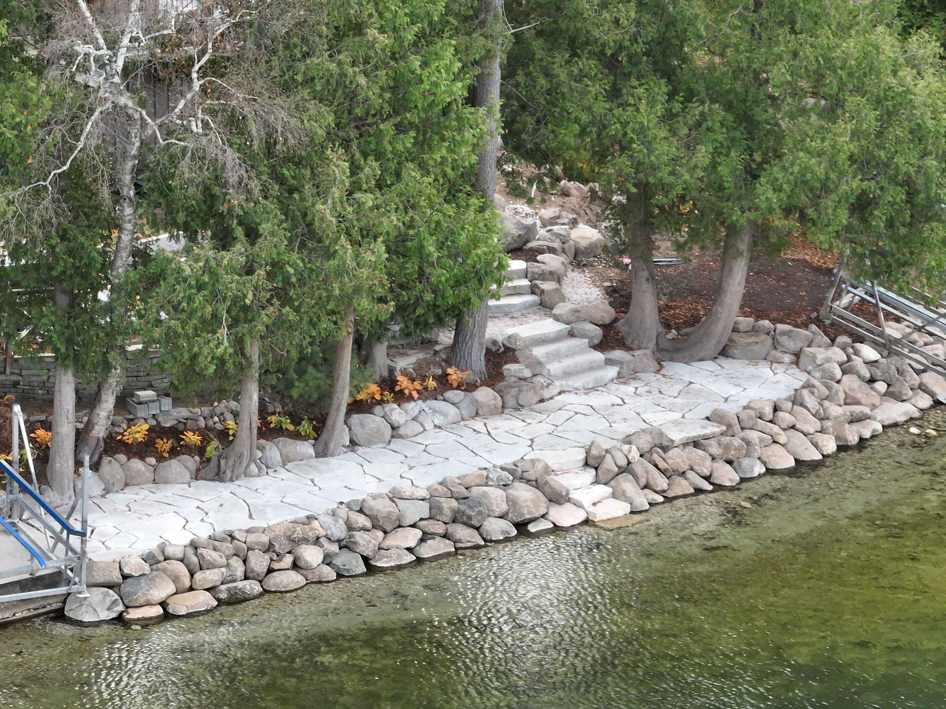 A stone walkway and staircase built into a shoreline, nestled among trees and landscaping along a clear lake.