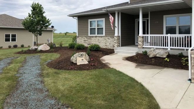 A modern brown and stone house with a front porch, landscaping, and a gravel walkway leading to the entrance.