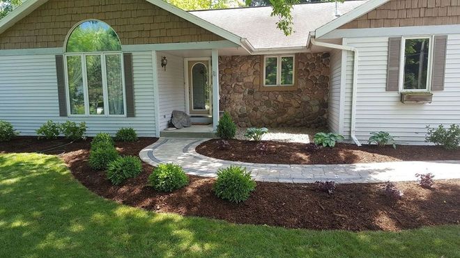 A house with white siding and stone accents, featuring a curved stone walkway leading to the front door, surrounded by mulch.