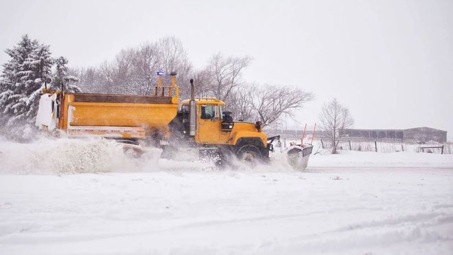 A yellow snowplow clearing snow from a road during a winter day.