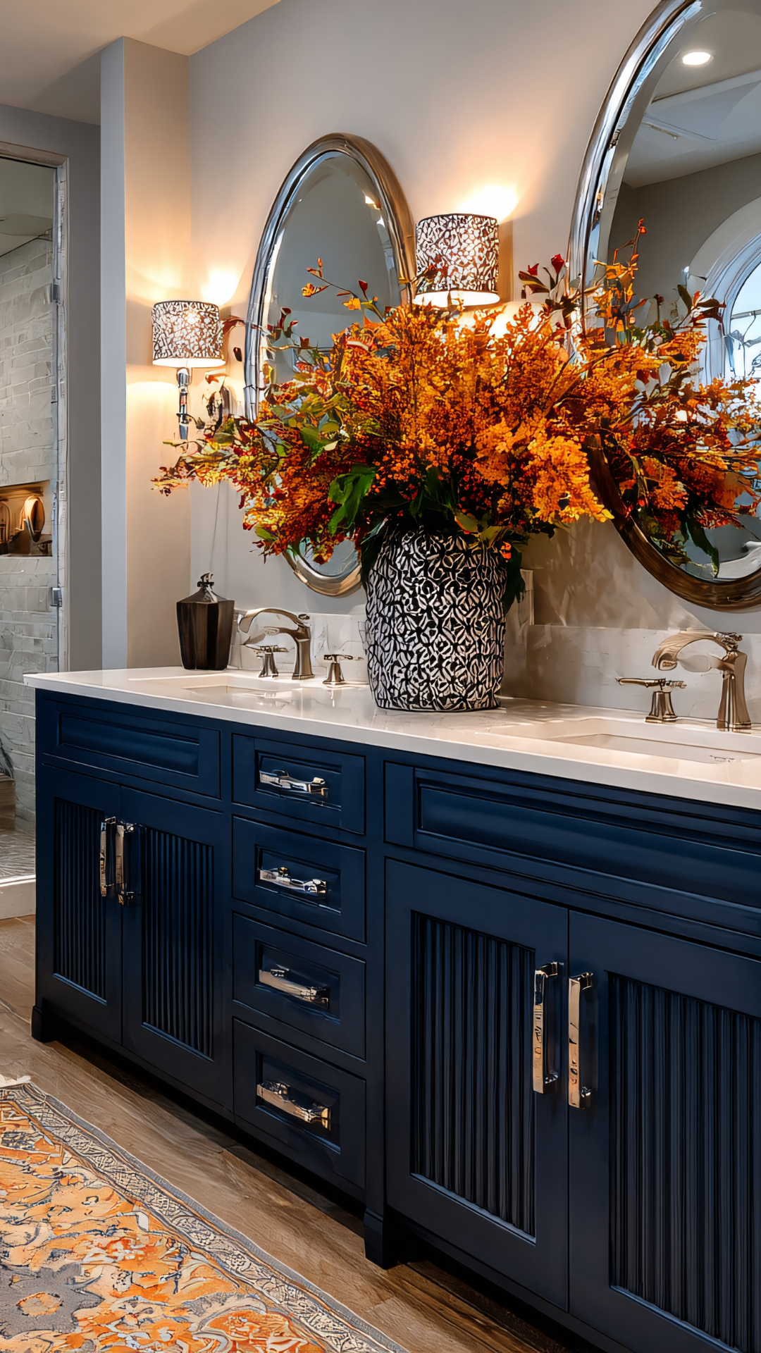 Navy blue bathroom vanity with silver hardware, oval mirrors, and orange floral arrangement.