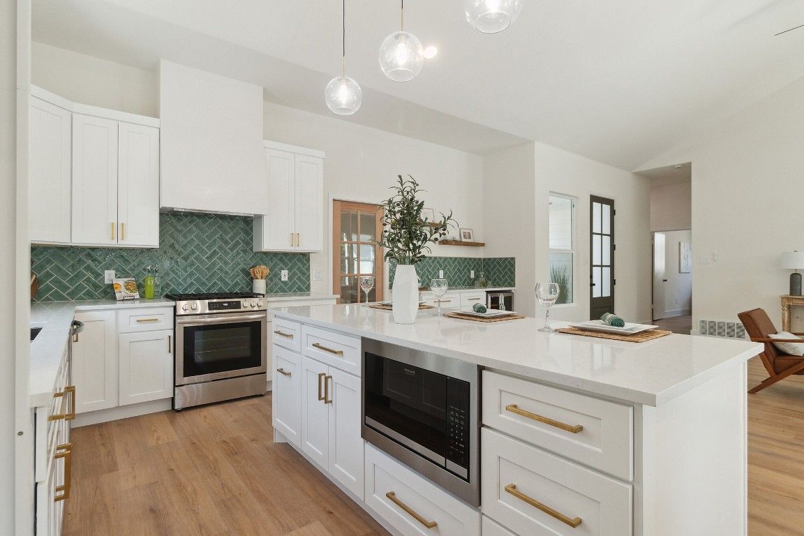 Modern white kitchen with island, stainless steel appliances, and green tile backsplash.