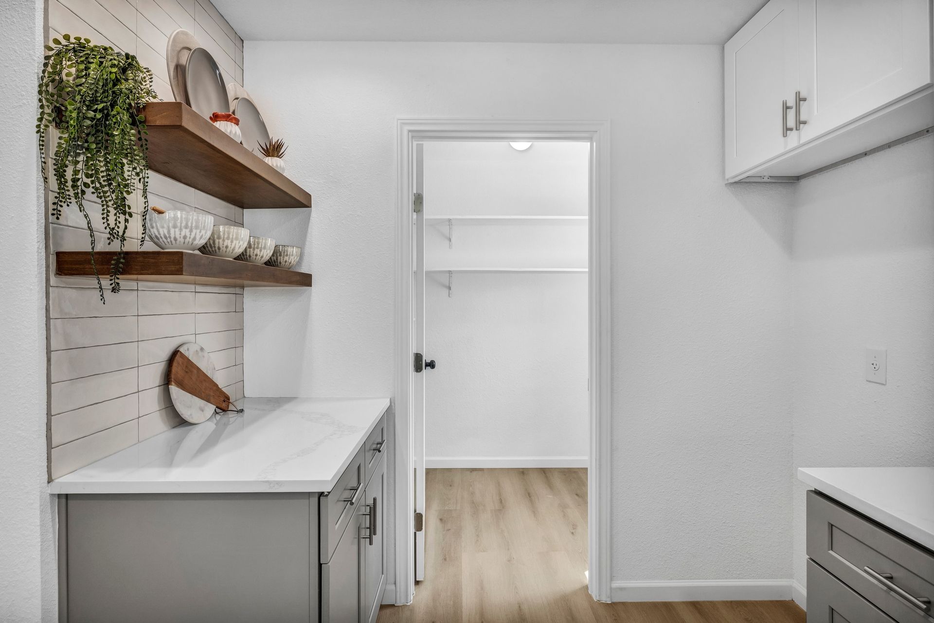 Kitchen with open pantry doorway, cabinets, floating shelves, and countertop.