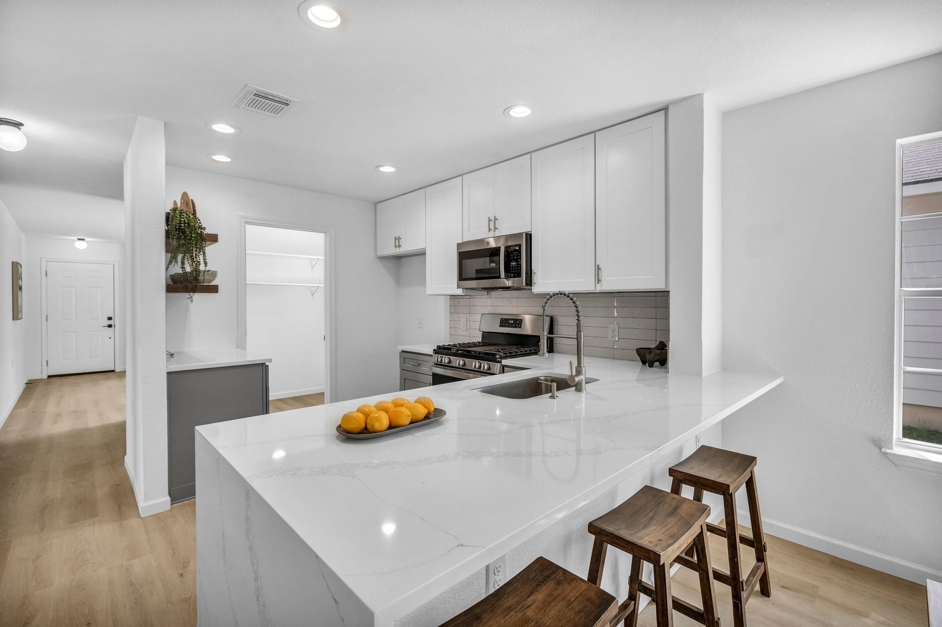 Modern white kitchen with island, stools, stainless steel appliances, and wooden floors.