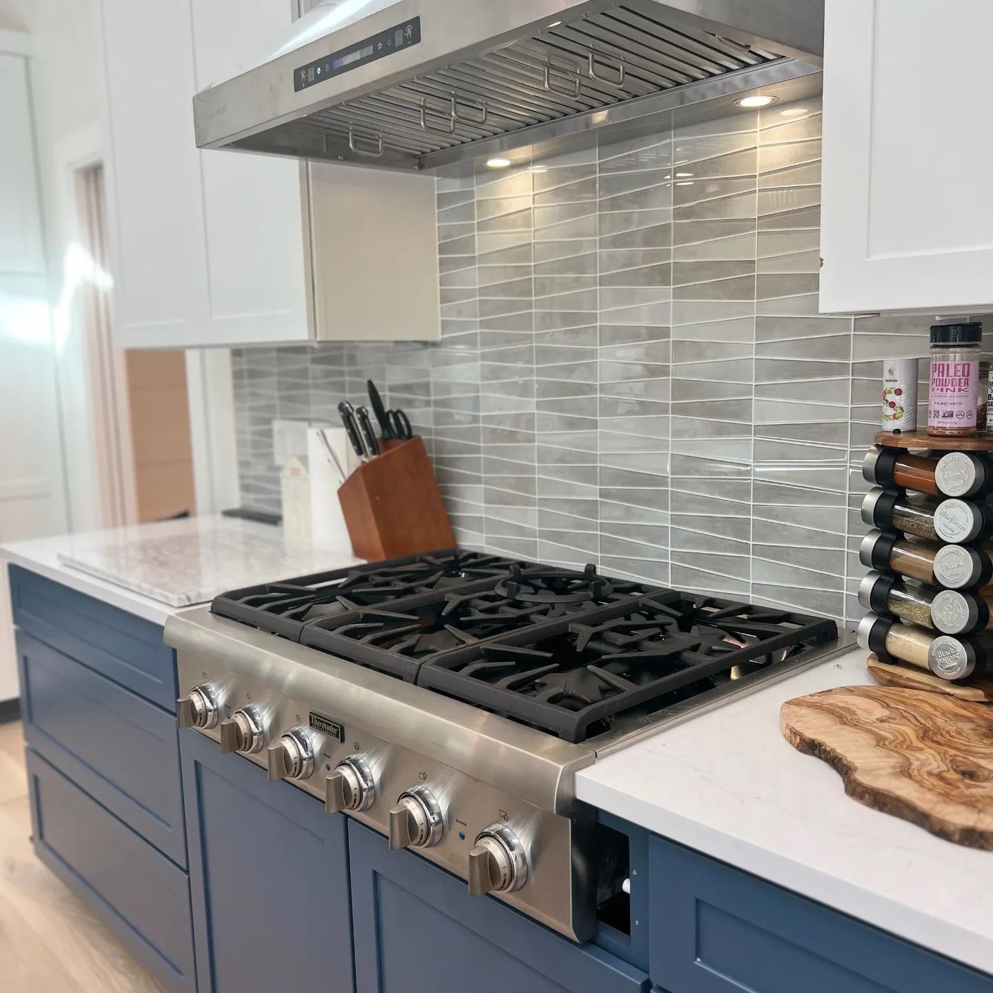 Kitchen with stainless steel range, blue cabinets, white countertops, and gray tile backsplash