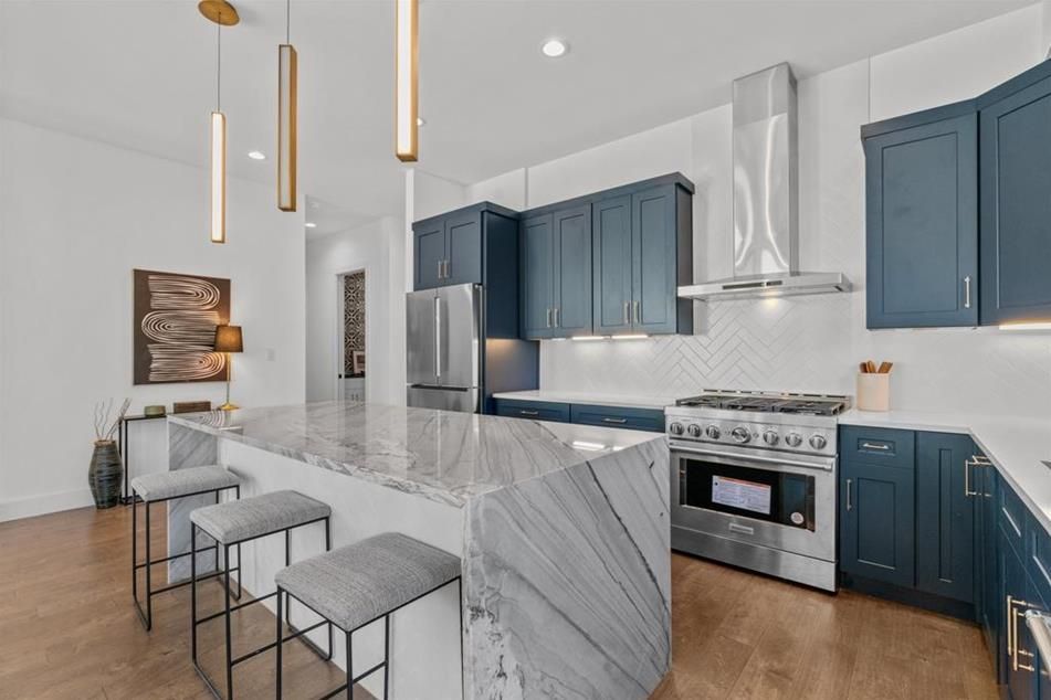Modern kitchen with blue cabinets, marble island, stainless steel appliances, and wooden floor.