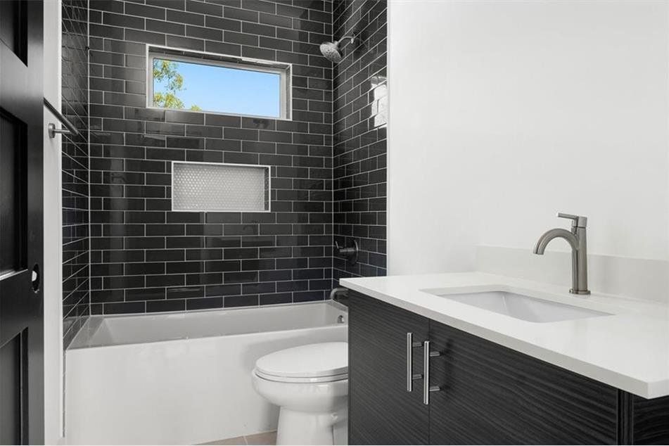 Modern bathroom with black tiled shower, white tub, white sink, and dark wood vanity.