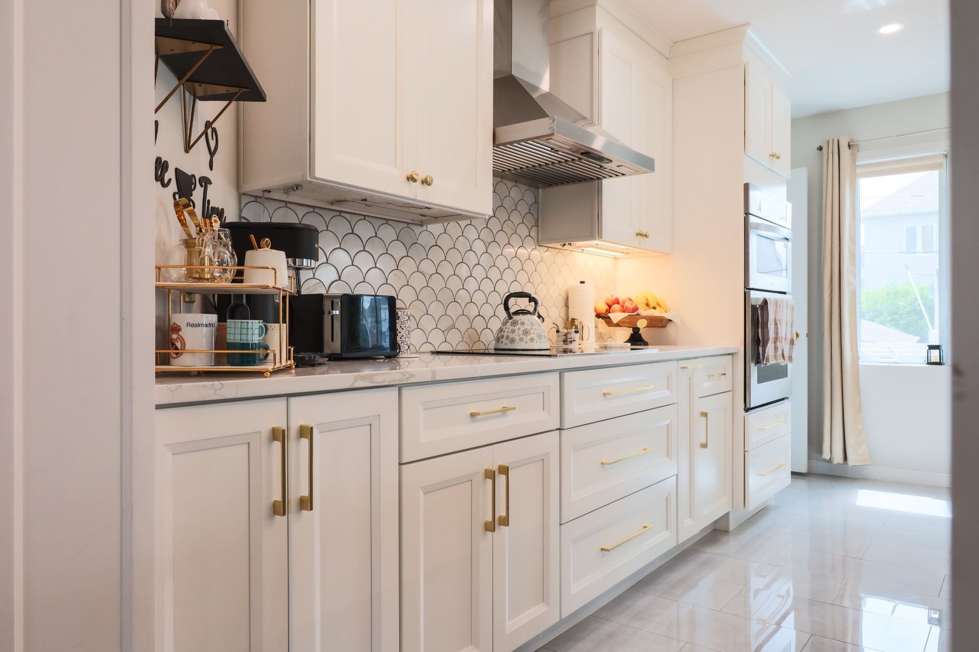 White kitchen with gold hardware, range hood, tiled backsplash, and built-in oven