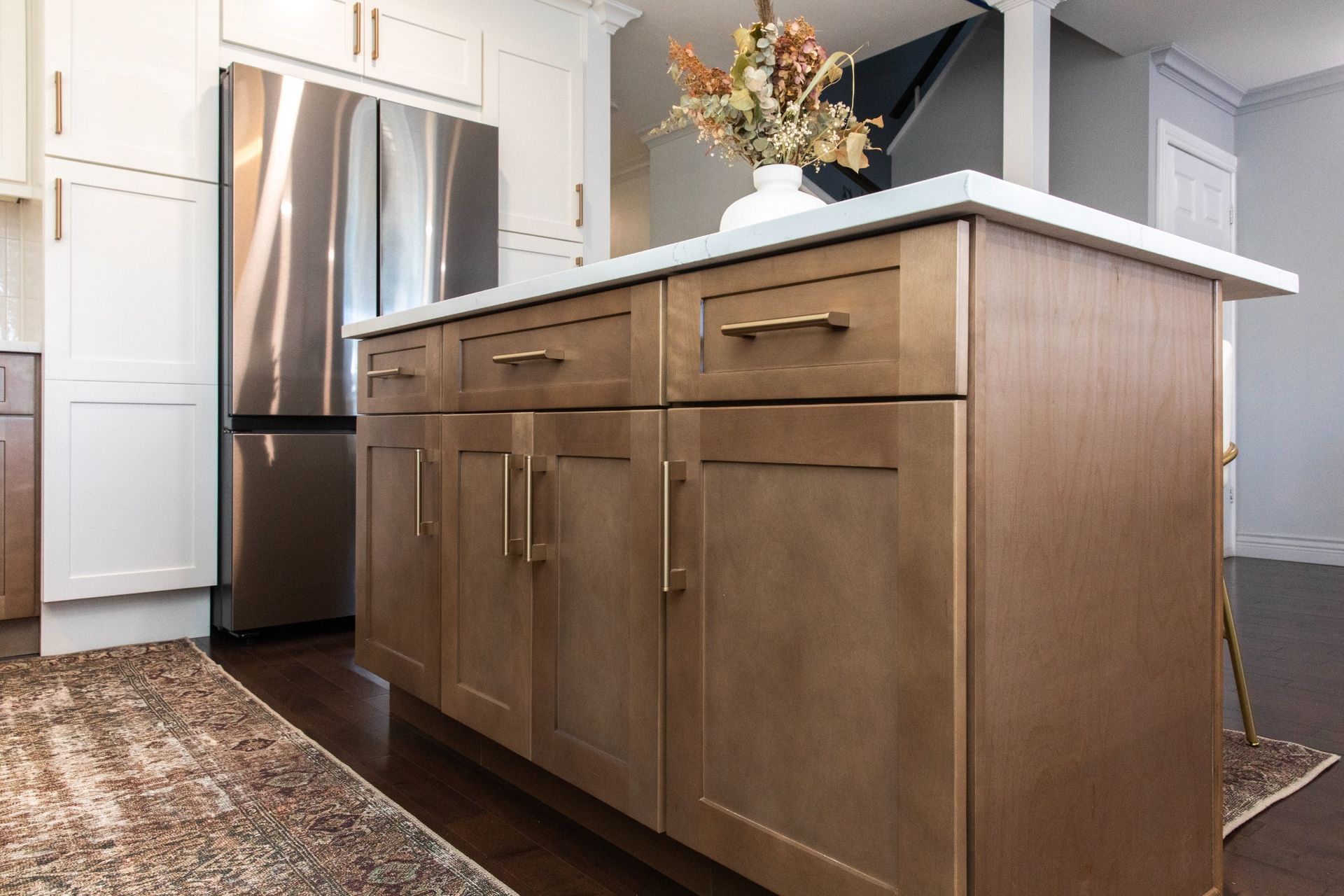 Kitchen island with wood-tone cabinets, white countertop, stainless steel fridge, and gold hardware