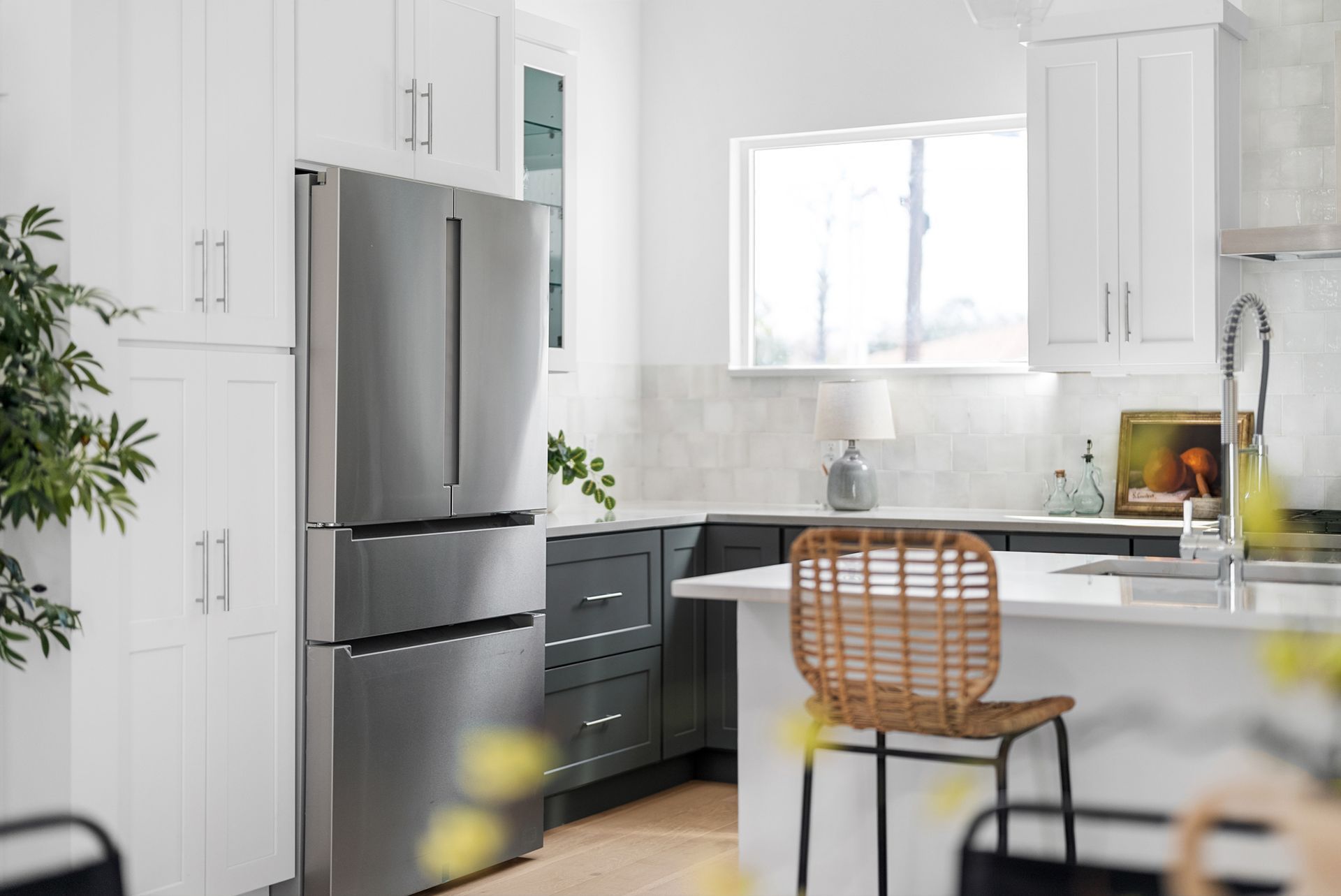 Modern kitchen with white and gray cabinets, stainless steel refrigerator, and wicker bar stool