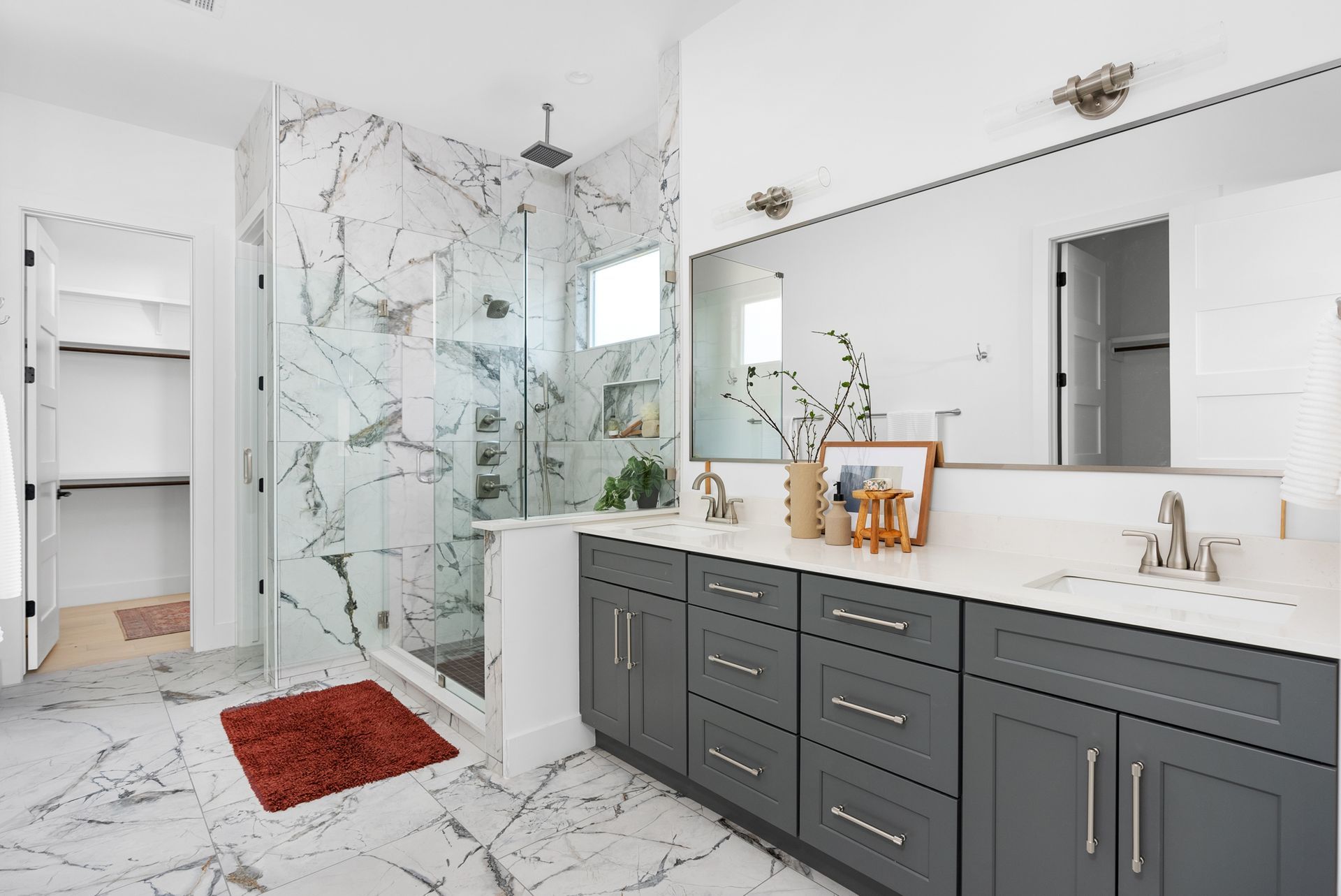 Modern bathroom with gray cabinets, marble shower, and double vanity.