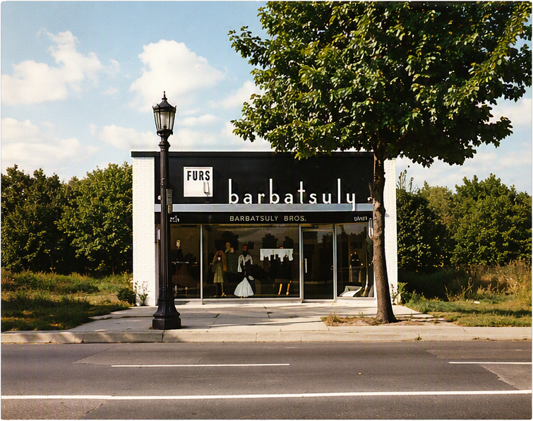 Small black-and-white storefront with a sign reading “barbatsu,” beside a lamp post and trees by the road