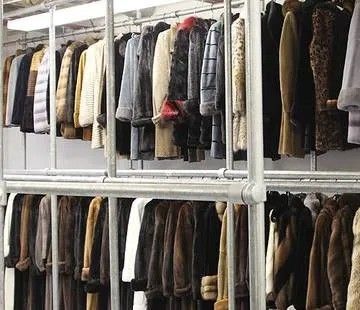Coats and jackets hanging on metal racks, organized in a clothing storage area.