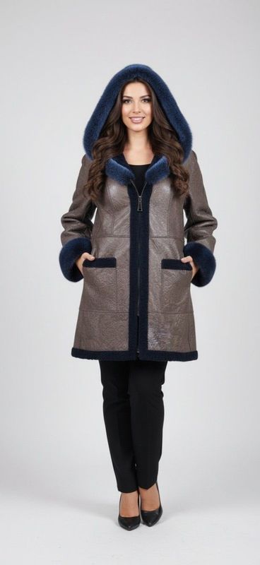 Woman wearing a brown hooded coat with blue trim, smiling, standing in front of a white background.